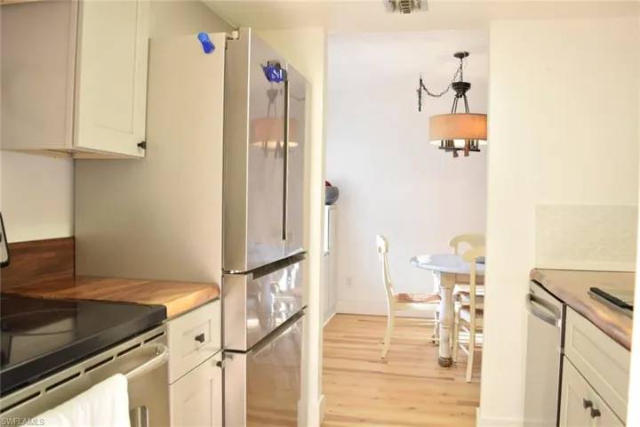 Stainless steel refrigerator in a kitchen featuring light wood-finish countertops and white cabinetry