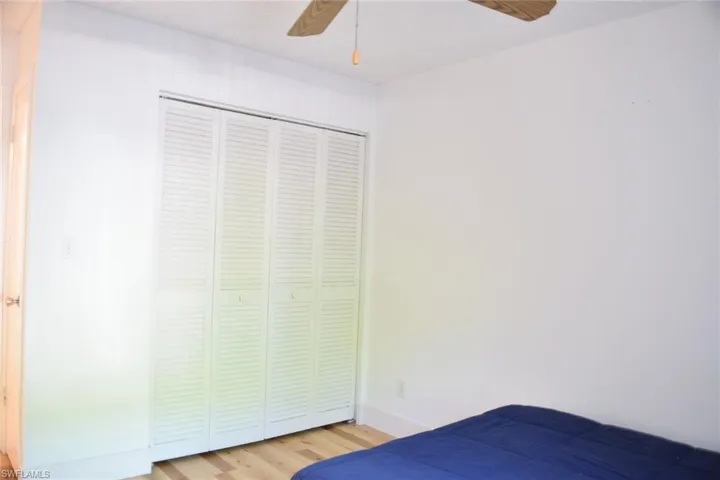 Bedroom featuring louvered bi-fold closet doors, light wood-finish flooring, and a ceiling fan with wood-finish blades