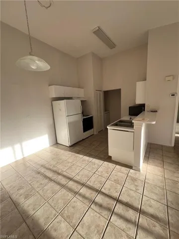 Kitchen with white appliances, decorative light fixtures, white cabinetry, light tile patterned flooring, and a high ceiling