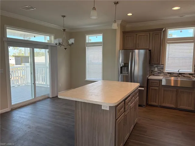 Kitchen featuring stainless steel fridge with ice dispenser, light countertops, a kitchen island, ornamental molding, and decorative backsplash