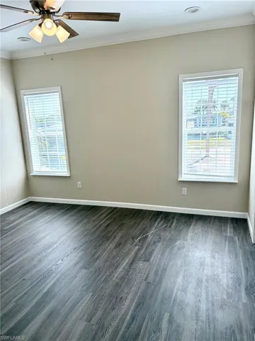 Empty room with ornamental molding, ceiling fan, and dark wood finished floors