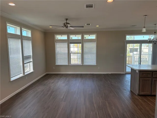 Unfurnished living room featuring dark wood-style flooring, ceiling fan, ornamental molding, and a chandelier