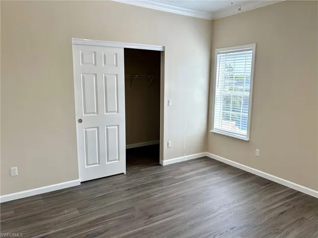Unfurnished bedroom with ornamental molding, dark wood-style floors, and a walk in closet