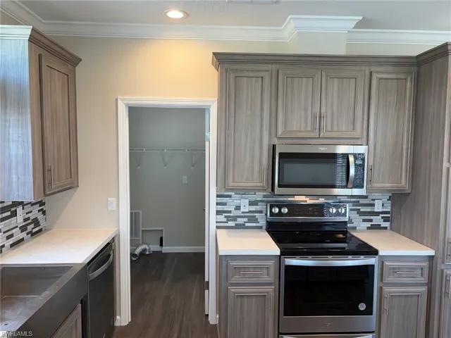 Kitchen with stainless steel appliances, decorative backsplash, light countertops, ornamental molding, and dark wood-style flooring