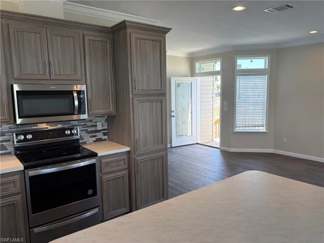Kitchen featuring stainless steel appliances, light countertops, crown molding, dark wood finish cabinetry, and recessed lighting