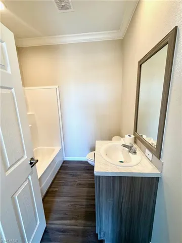 Full bathroom with vanity, dark wood-type flooring, ornamental molding, and  shower combination