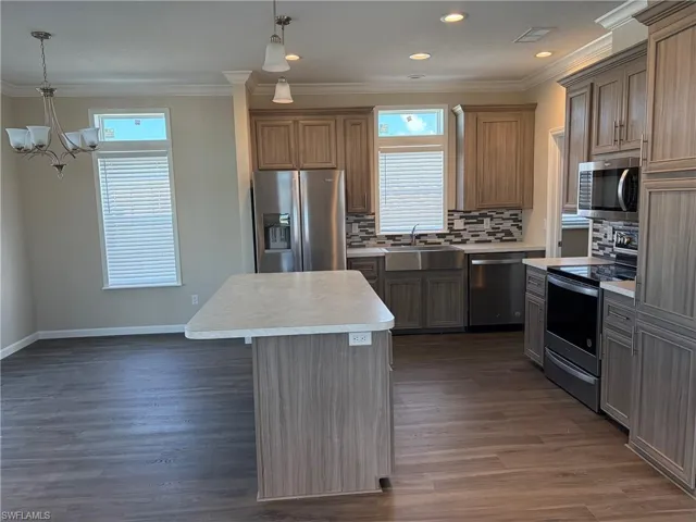 Kitchen with stainless steel appliances, backsplash, light countertops, a kitchen island, and crown molding