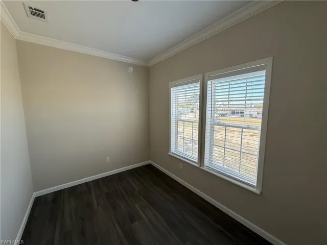 Spare room featuring dark wood-style flooring and crown molding