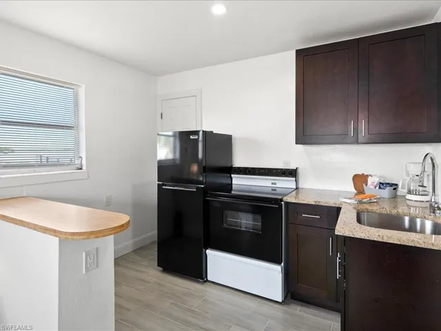 Kitchen with black appliances, dark wood finish cabinets, wood tiled floors, light stone counters, and recessed lighting