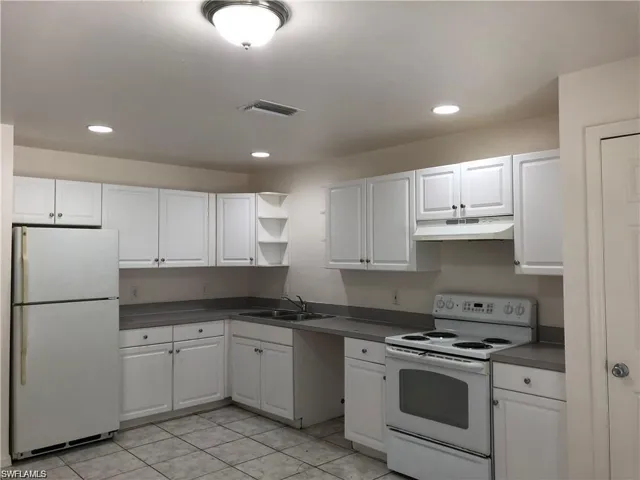 Kitchen with white appliances, under cabinet range hood, white cabinets, dark countertops, and recessed lighting