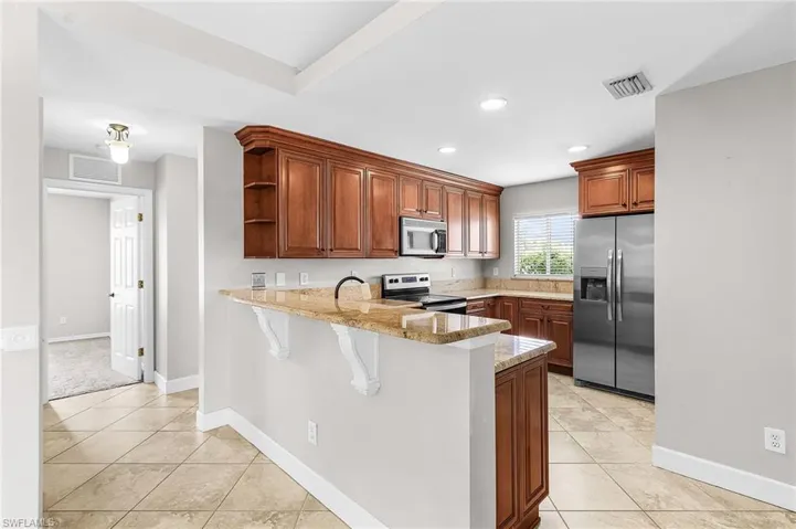 Kitchen featuring appliances with stainless steel finishes, a breakfast bar, light stone countertops, a peninsula, and brown cabinets