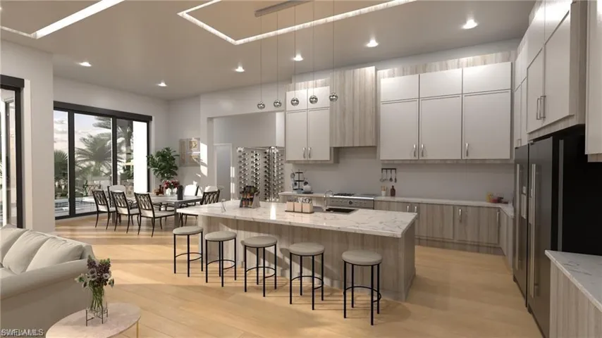 Kitchen featuring two tone cabinetry, a kitchen bar, light wood-style floors, light stone counters, and an island with sink