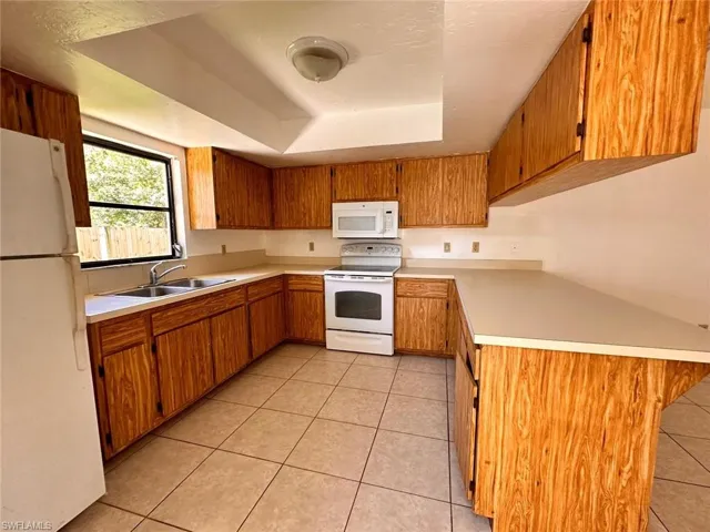 Kitchen with light tile patterned floors, white appliances, sink, and a raised ceiling