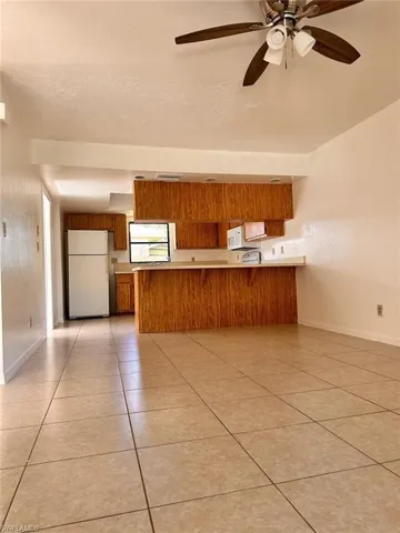 Kitchen featuring ceiling fan, kitchen peninsula, light tile patterned flooring, and white appliances