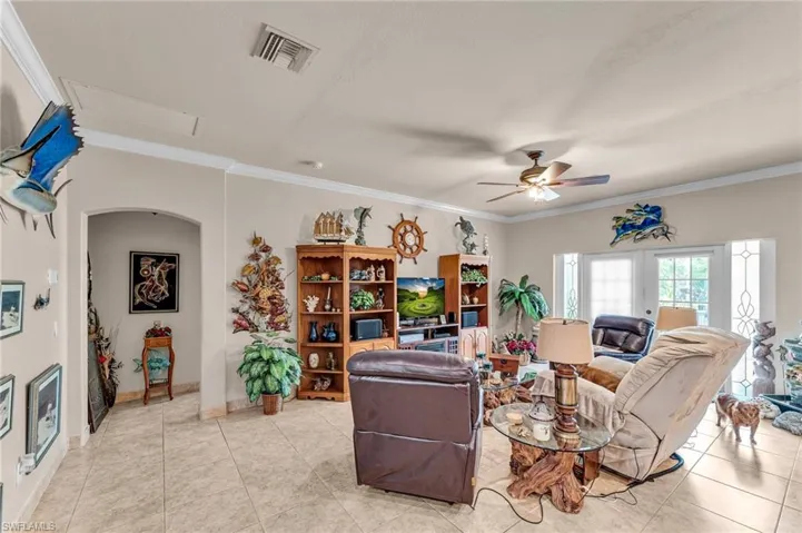 Living room with ceiling fan, light tile patterned floors, crown molding, and french doors