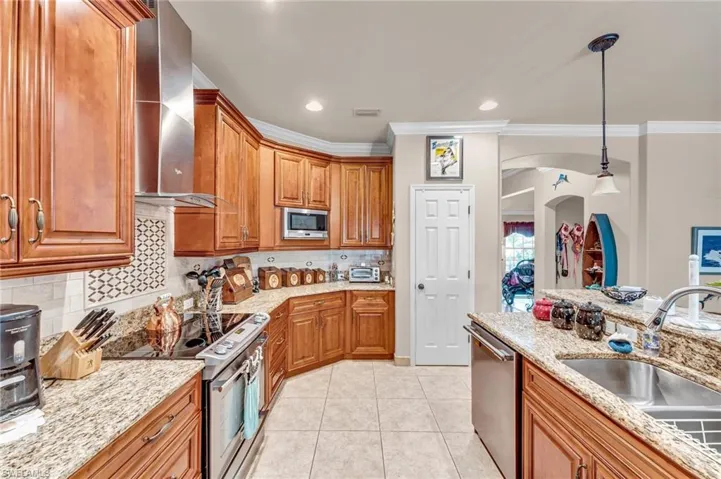Kitchen featuring decorative light fixtures, appliances with stainless steel finishes, light stone counters, sink, and wall chimney range hood