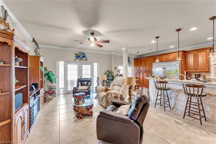 Living room featuring ceiling fan, light tile patterned floors, decorative columns, and crown molding