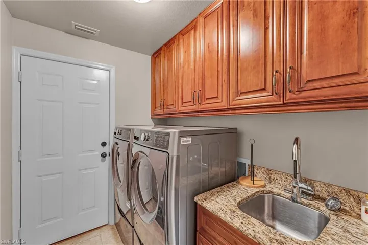 Laundry area with cabinets, a textured ceiling, light tile patterned floors, washing machine and dryer, and sink