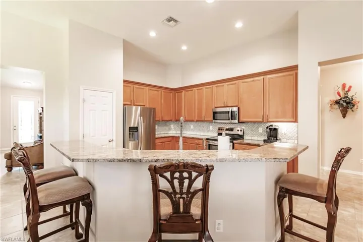 Kitchen featuring tasteful backsplash, light tile flooring, light stone counters, and stainless steel appliances