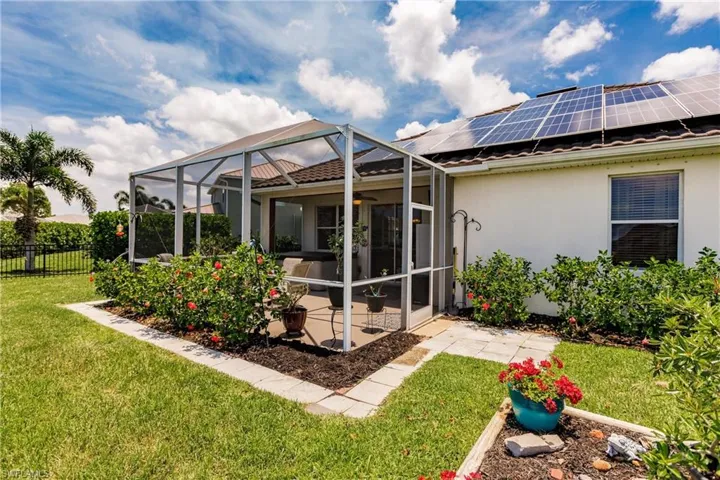 Back of house with a lanai, solar panels, and a lawn