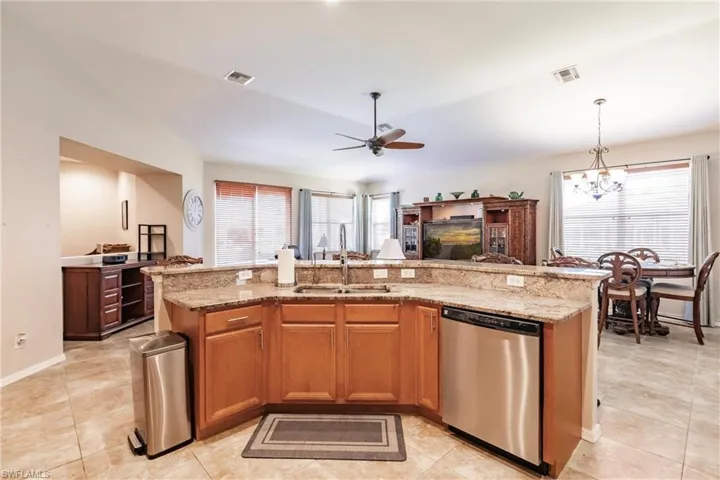 Kitchen with ceiling fan with notable chandelier, light stone counters, pendant lighting, sink, and dishwasher