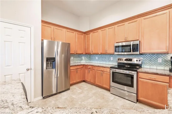 Kitchen featuring stainless steel appliances, light tile floors, light stone counters, and backsplash
