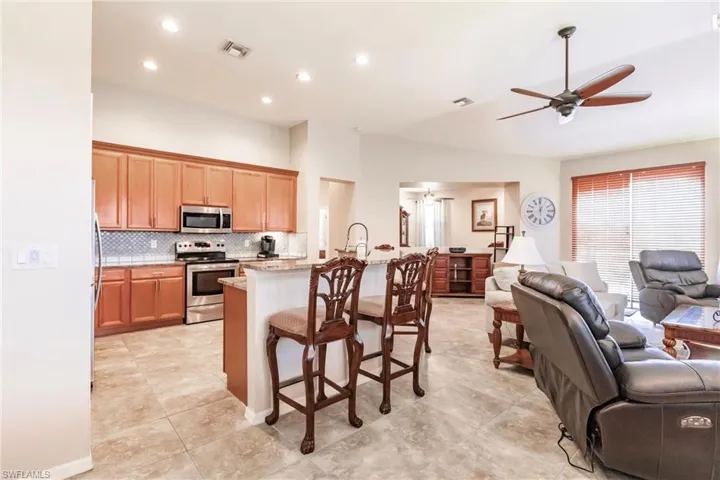 Kitchen featuring a kitchen breakfast bar, electric stove, backsplash, ceiling fan, and light tile floors