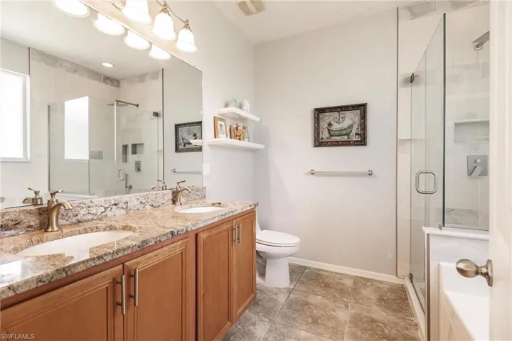 Bathroom featuring double vanity, an enclosed shower, toilet, and tile floors