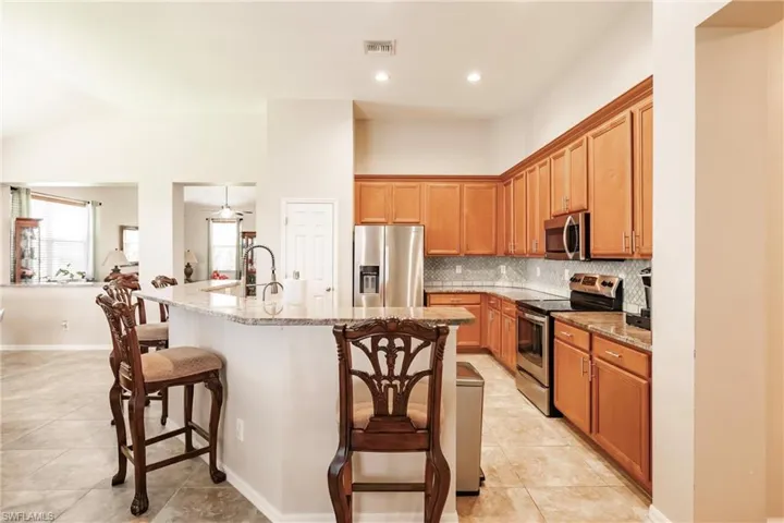 Kitchen with appliances with stainless steel finishes, an island with sink, light stone counters, a kitchen bar, and light tile floors