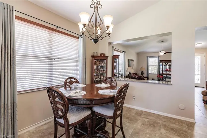 Dining room with ceiling fan with notable chandelier, light tile flooring, and lofted ceiling
