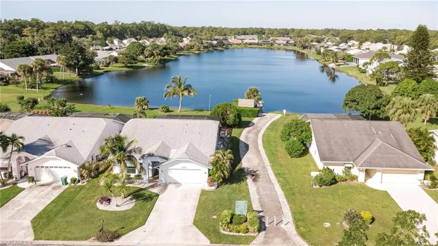 Aerial view of path to dock and community lake featuring a waterfront setting, concrete driveways, manicured lawns, and palm tree landscaping