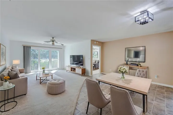Virtually staged open-concept great room, flex and dining area featuring neutral wall tones, tile flooring, wall-to-wall carpeting, a ceiling fan, and sliding glass doors leading to a balcony