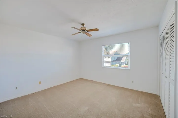 Vacant Guest Bedroom - Neutral-toned carpeting, white louvered closet doors, ceiling fan with light fixture, and horizontal blind window covering