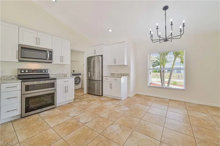 Kitchen with light stone countertops, stainless steel appliances, pendant lighting, washer / dryer, and an inviting chandelier