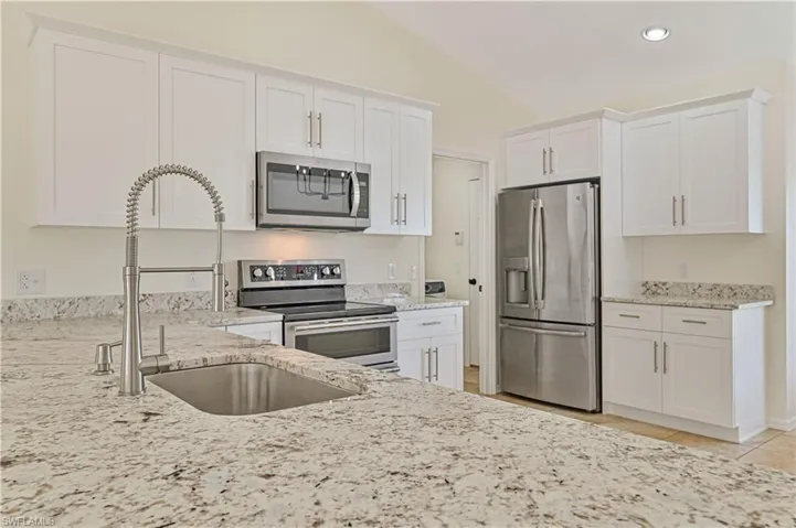 Kitchen with white cabinets, light tile flooring, vaulted ceiling, and stainless steel appliances