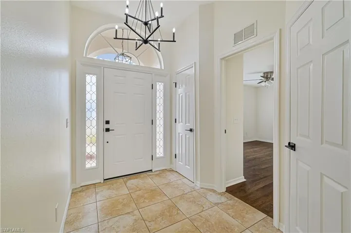 Foyer entrance featuring a wealth of natural light, lofted ceiling, light wood-type flooring, and ceiling fan with notable chandelier