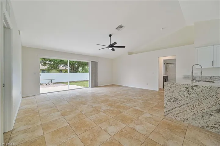 Unfurnished living room featuring sink, ceiling fan, light tile flooring, and lofted ceiling