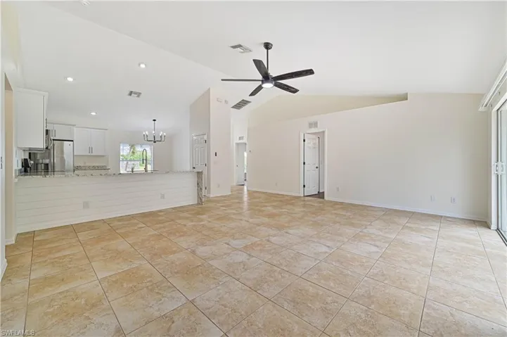 Unfurnished living room with ceiling fan with notable chandelier, lofted ceiling, and light tile floors