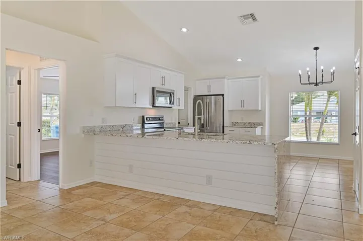 Kitchen with white cabinetry, light stone countertops, appliances with stainless steel finishes, sink, and light tile flooring