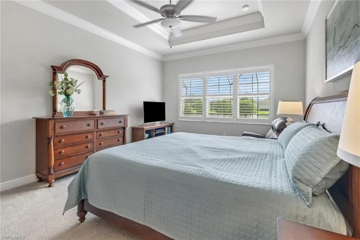 Bedroom with light colored carpet, ceiling fan, ornamental molding, and a raised ceiling