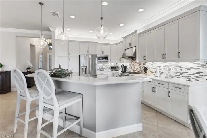 Kitchen featuring a breakfast bar area, a center island with sink, pendant lighting, light tile patterned floors, and appliances with stainless steel finishes