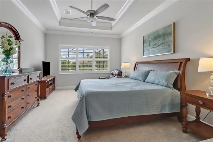 Carpeted bedroom with crown molding, ceiling fan, and a raised ceiling