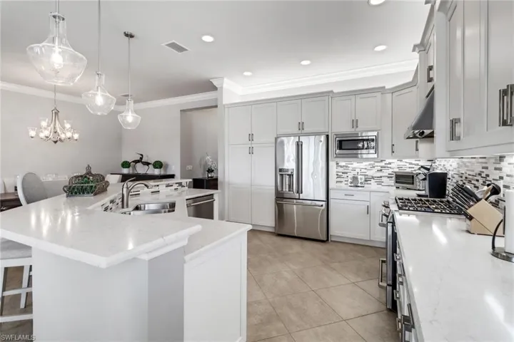 Kitchen with appliances with stainless steel finishes, light stone counters, sink, a breakfast bar area, and pendant lighting