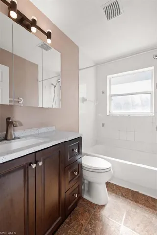 Bathroom with vanity, shower / bathtub combination, and dark stone finish floors
