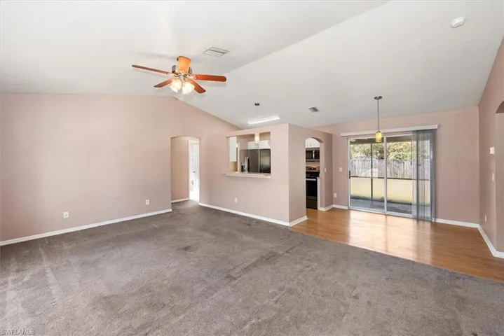 Unfurnished living room featuring arched walkways, light colored carpet, vaulted ceiling, and a ceiling fan