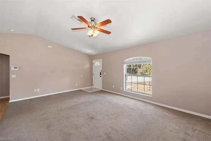 Empty room featuring vaulted ceiling, a ceiling fan, and light colored carpet