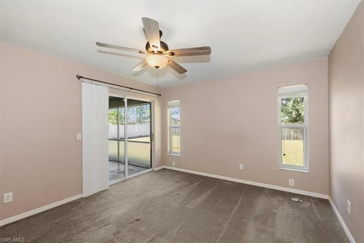 Empty room with dark colored carpet, plenty of natural light, and ceiling fan