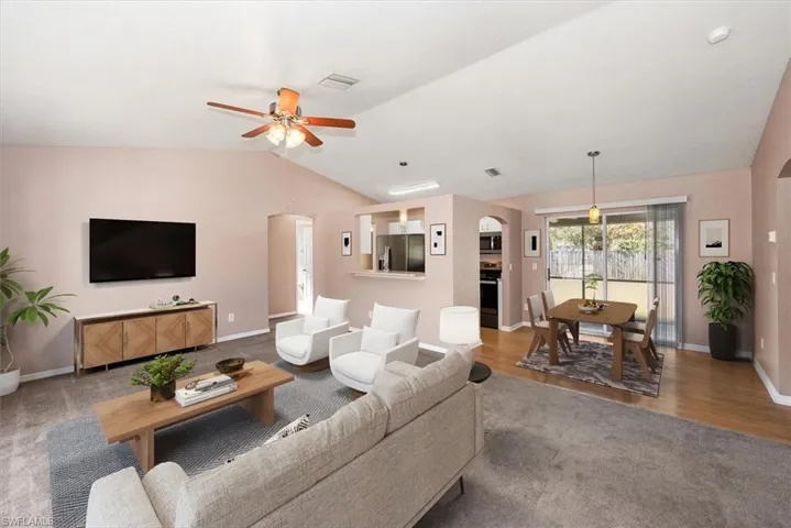 Carpeted living room with arched walkways, lofted ceiling, and a ceiling fan