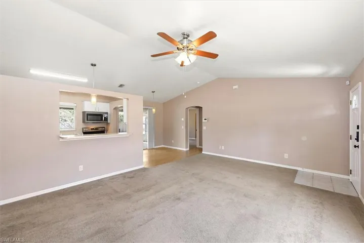 Unfurnished living room with arched walkways, lofted ceiling, light carpet, and ceiling fan