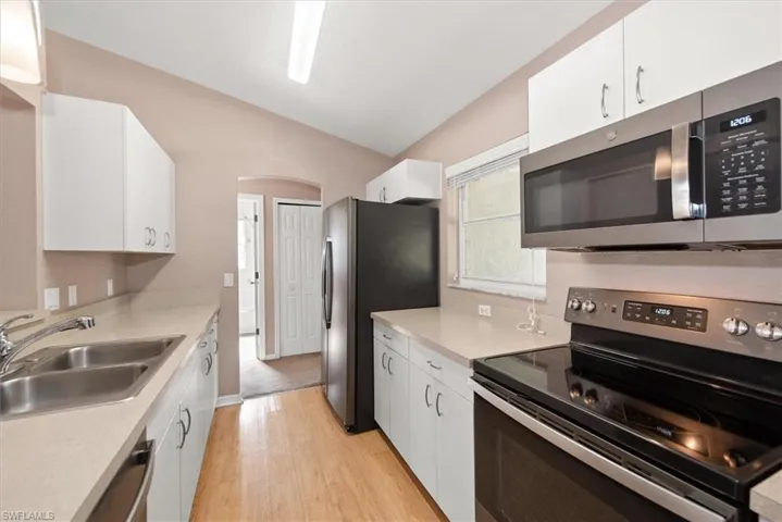 Kitchen featuring stainless steel appliances, white cabinetry, light countertops, vaulted ceiling, and light wood-style flooring